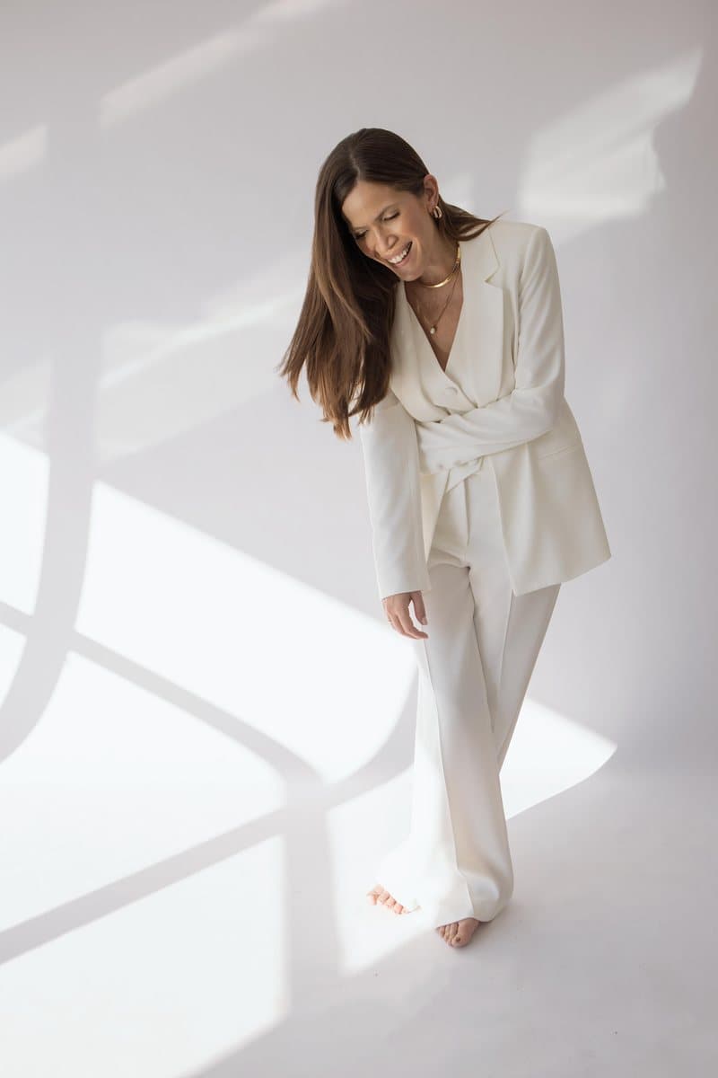 Nina Hayashi de terno claro, sorrindo e olhando para baixo, em estúdio