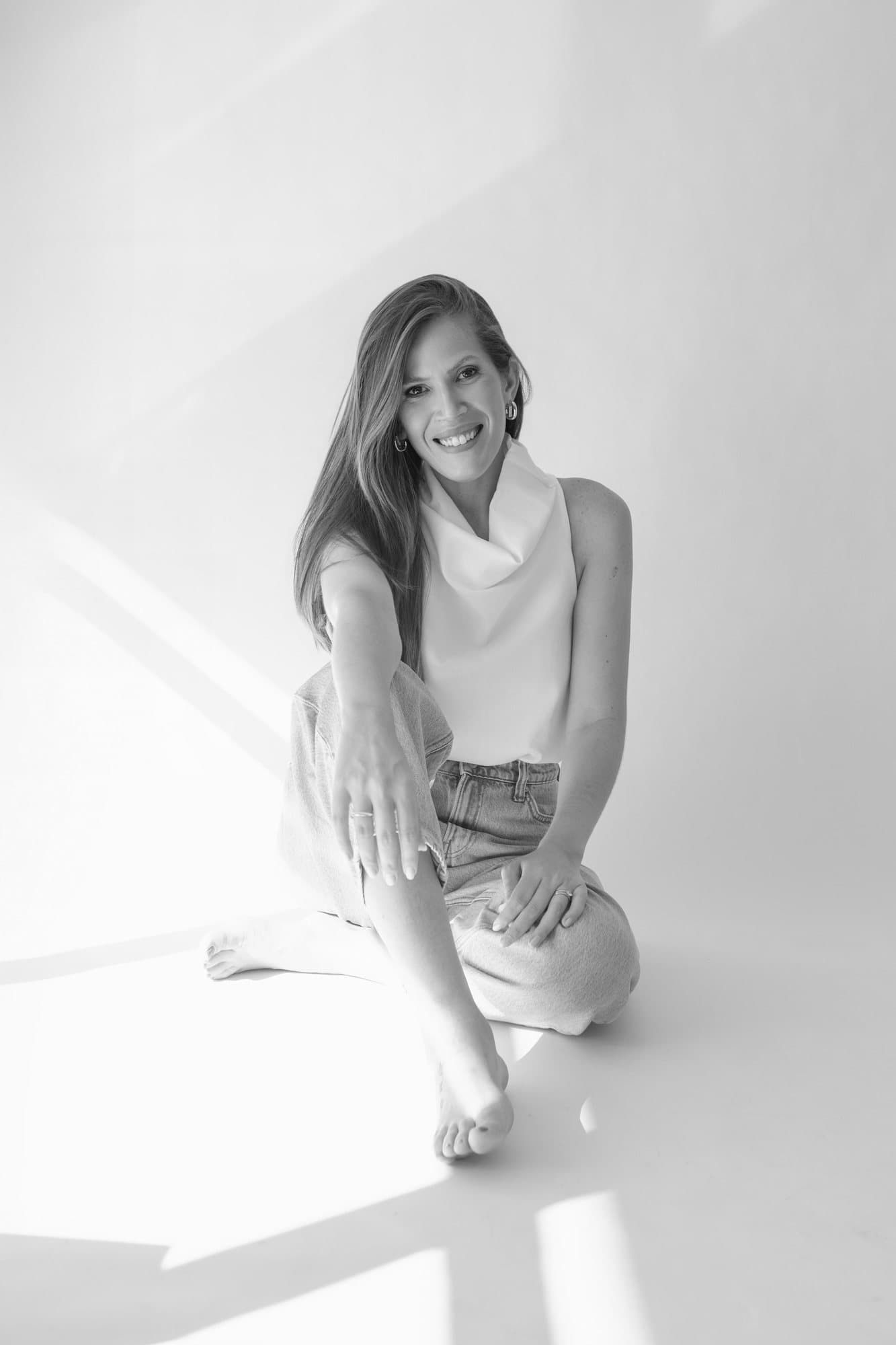 Retrato em preto e branco de Nina Hayashi sentada no chão do estúdio, sorrindo